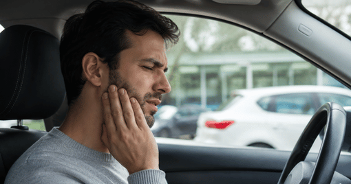 Man sitting in a parked car holding his jaw in discomfort